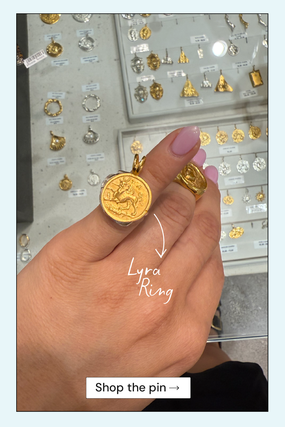 Hand wearing a gold ring with 'Lyra Ring' text, set against a jewelry display background.