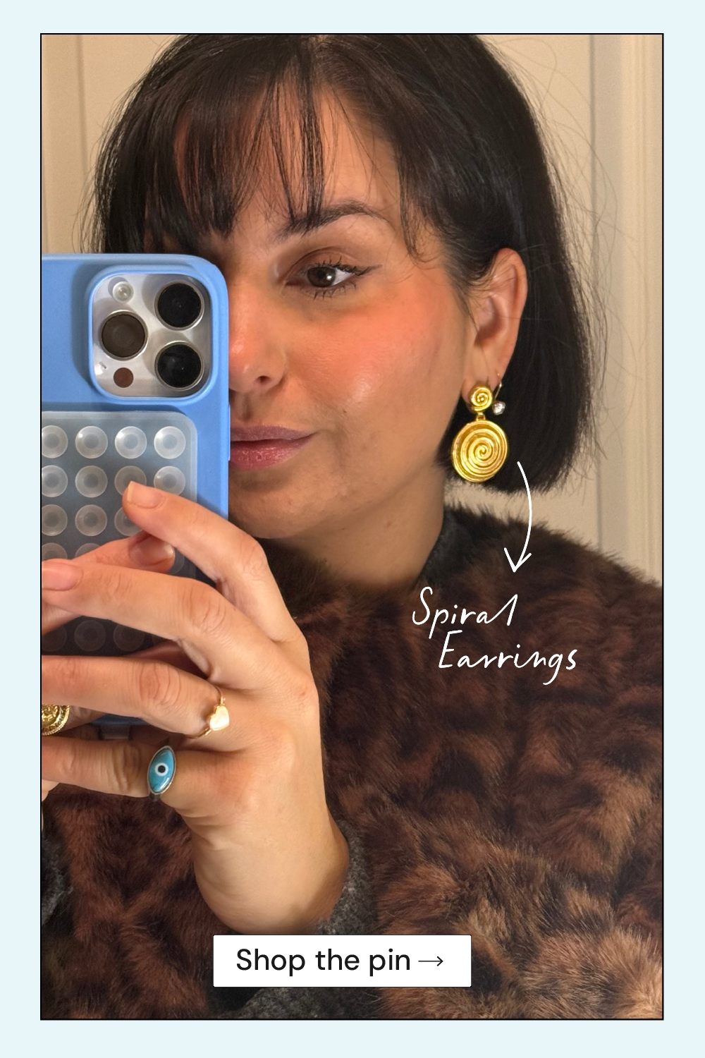 Woman wearing spiral earrings taking a mirror selfie, with text pointing to the earrings and a 'Shop the pin' link.